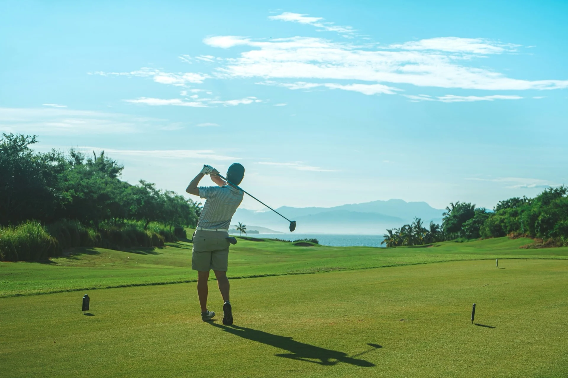 A golfer finishing a shot on a coastal course