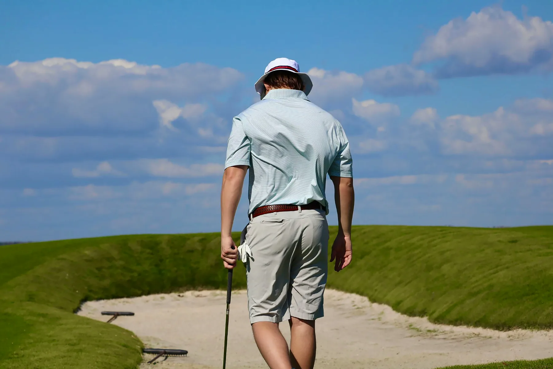 A golfer walking beside a bunker