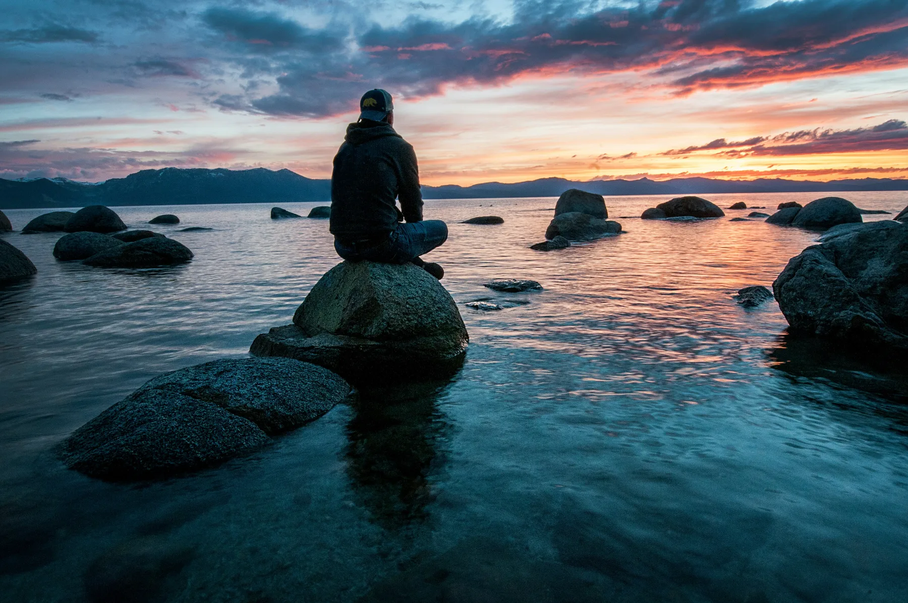 A person sitting beside a lake at sunset